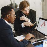 Two business professionals discuss marketing data on a laptop in a modern office.