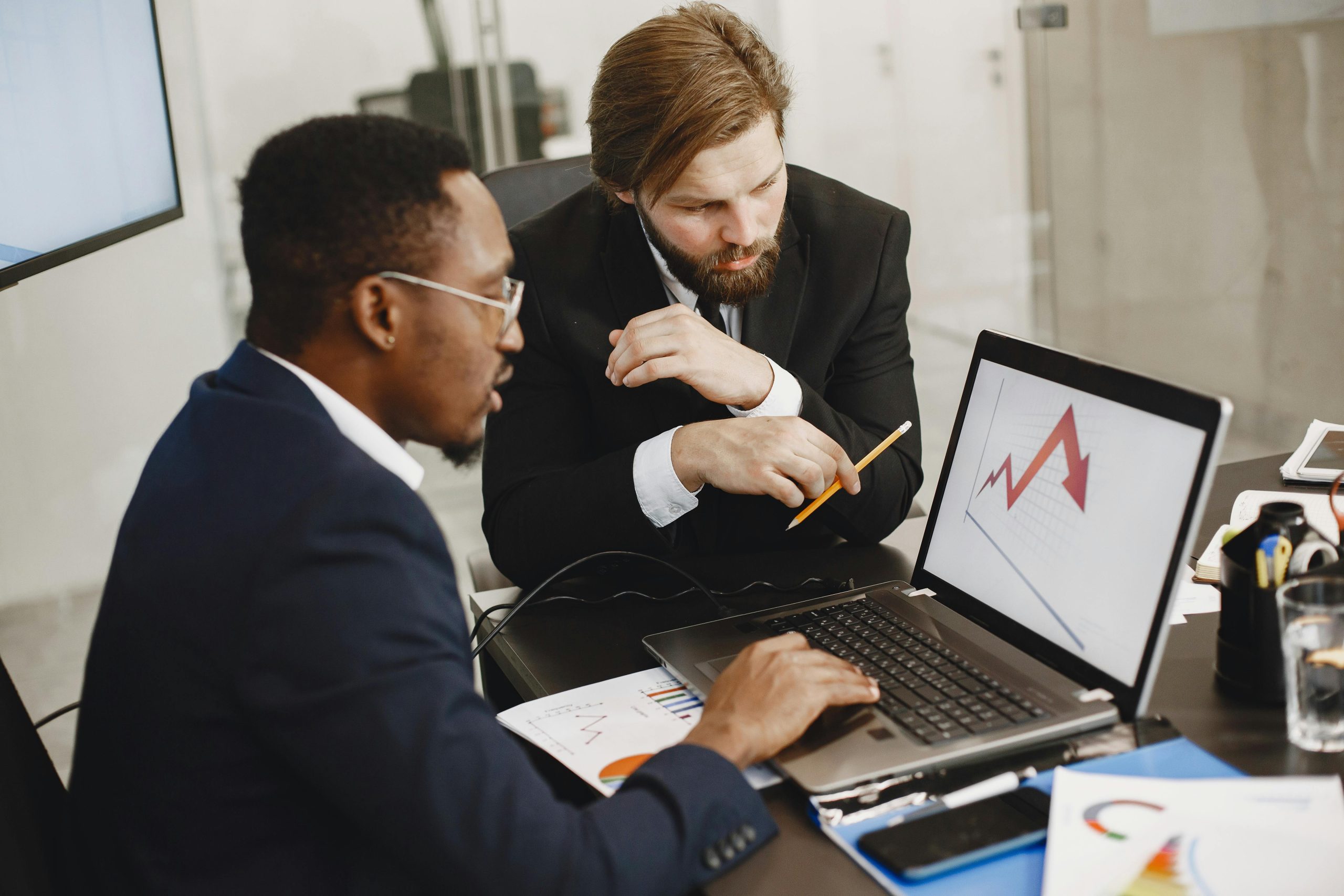 About Two business professionals discuss marketing data on a laptop in a modern office.